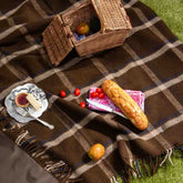Luxury wool waterproof picnic blanket in brown checkmate pattern, styled with picnic food and wicker basket on grass—perfect for outdoor dining and countryside picnics.